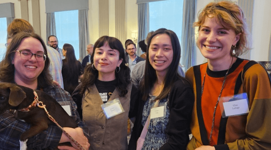 Elise LeSage stands in a row with 3 smiling women at a university events.