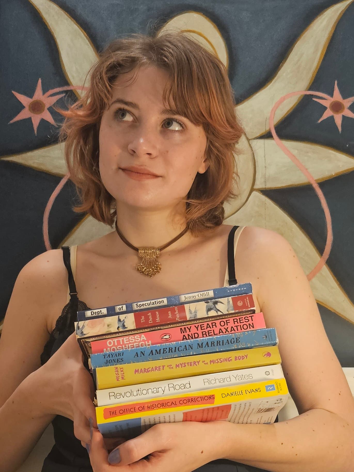 Elise LeSage is holding a stack of novels in front of an abstract painting.